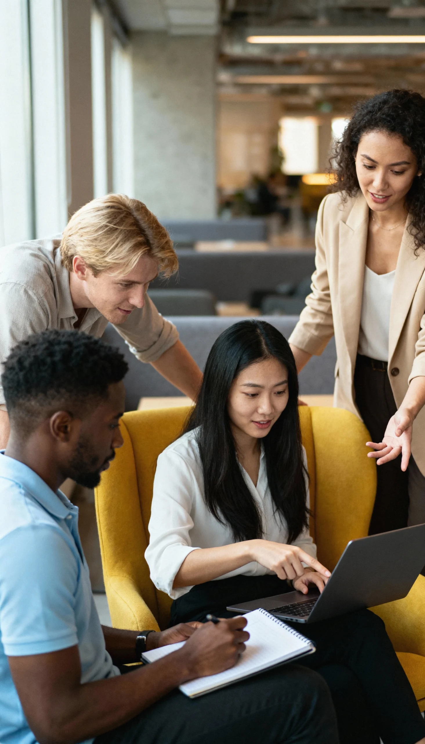 A group of professionals collaborating around a laptop in a modern office lounge, reviewing data and insights together to drive informed business decisions.
