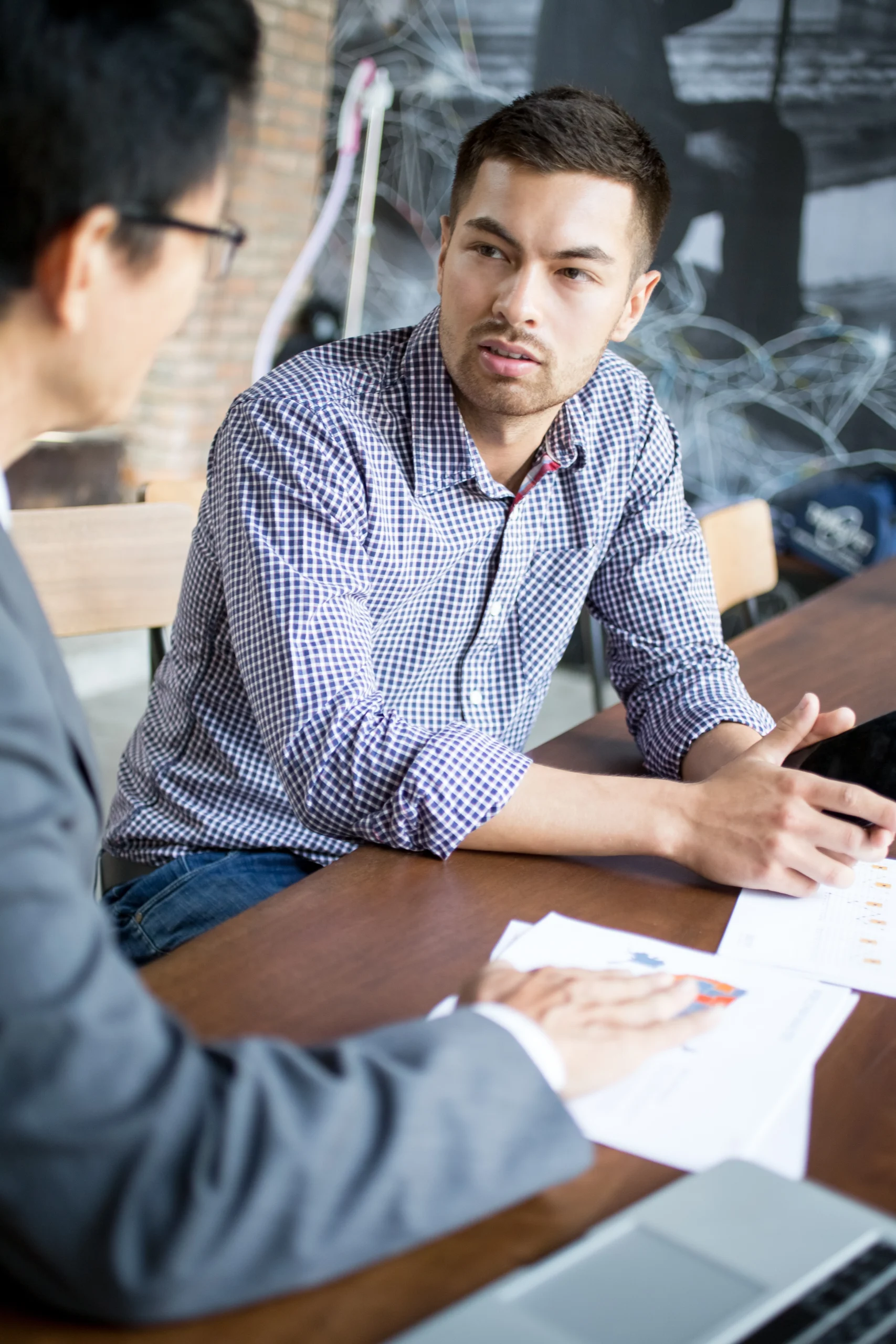 A professional in a blue checkered shirt engaged in a focused conversation with a colleague in a modern office setting, representing customer-centric dialogue and team collaboration.