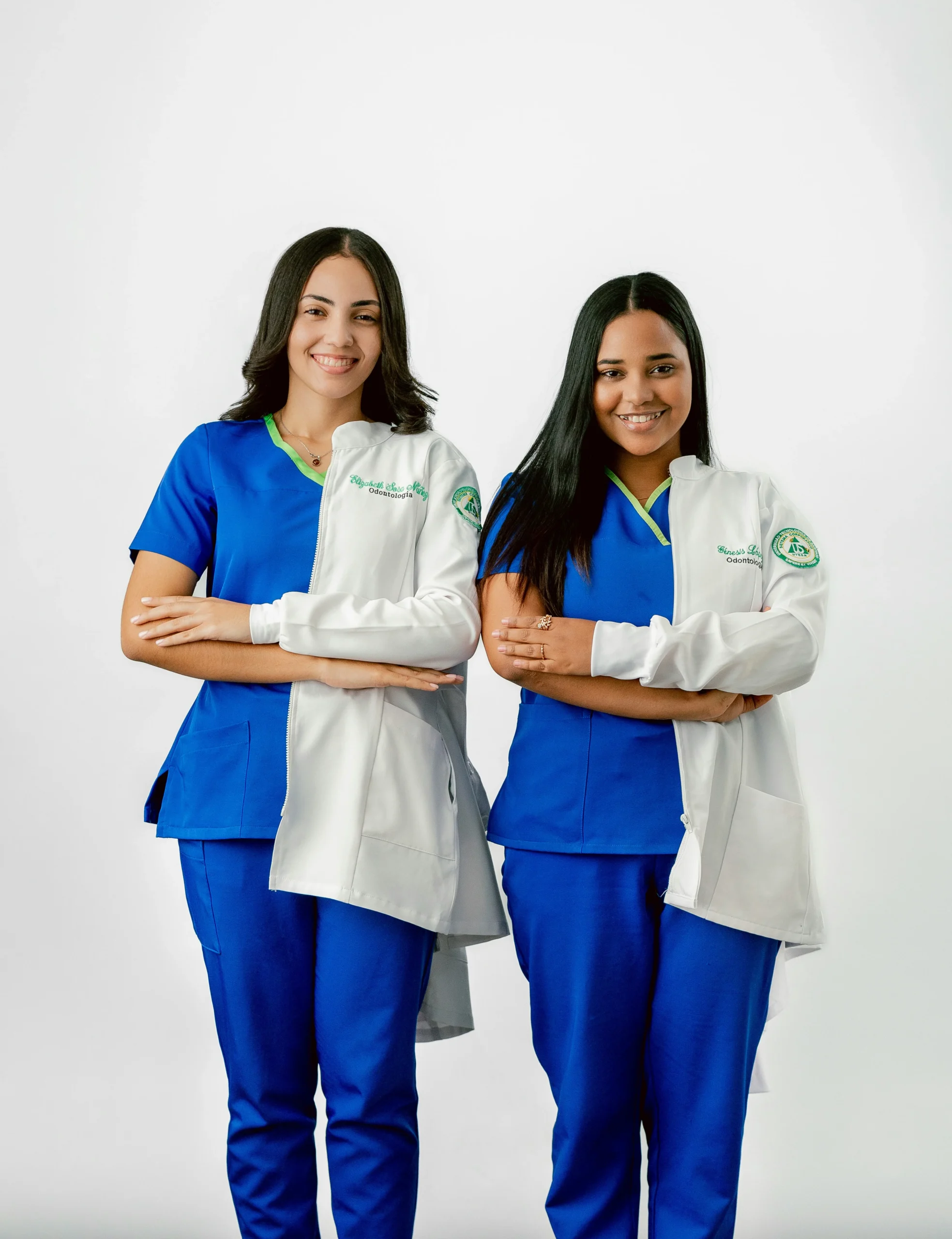 Two smiling healthcare professionals in matching blue scrubs and white coats standing confidently together, representing the consistent, friendly frontline teams whose service standards directly influence patient satisfaction, NPS, and health clinic growth.