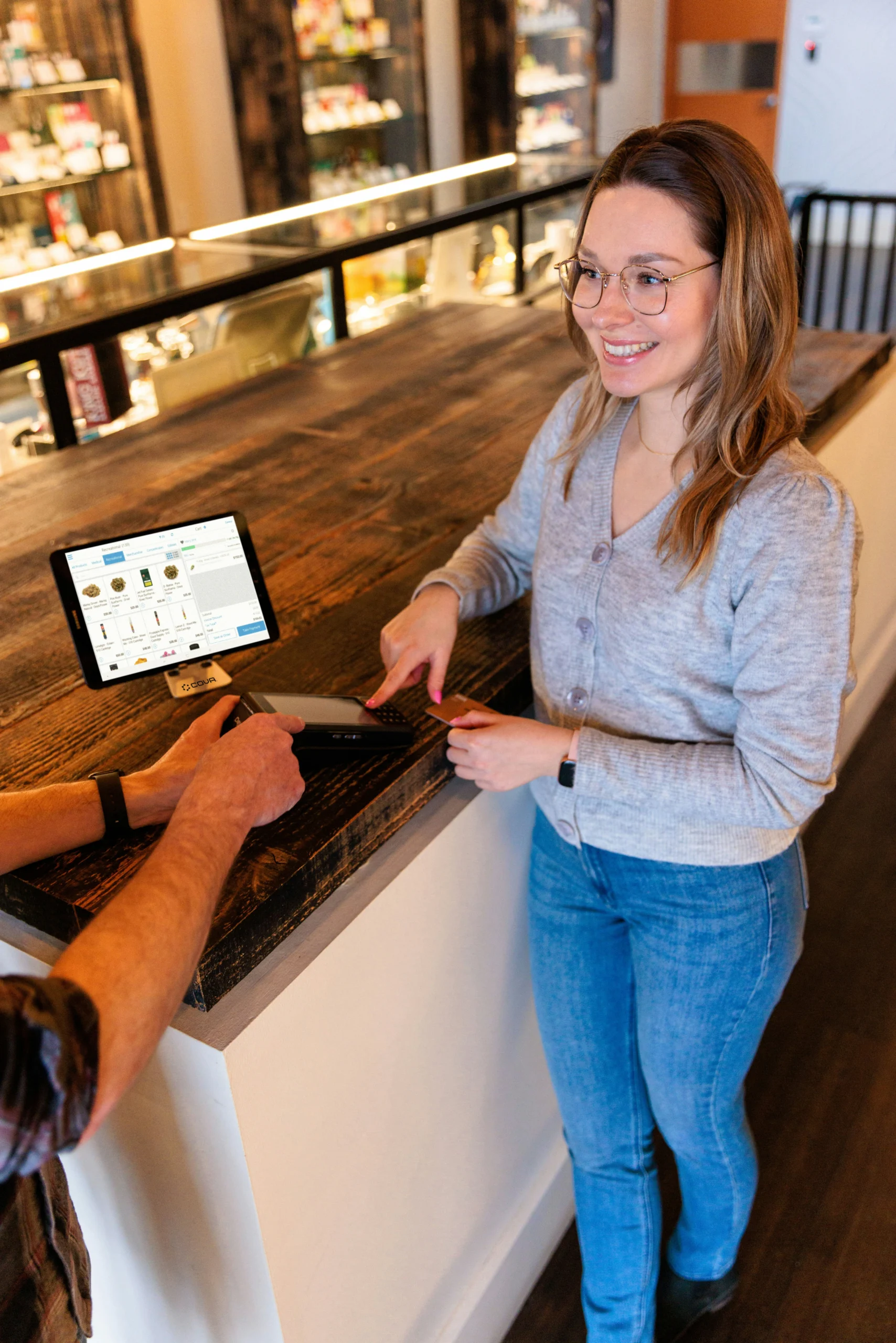 A smiling customer completing a card payment at a retail counter with a POS tablet system, representing a positive frontline service interaction and seamless in-store checkout experience.